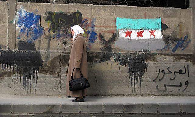 A Syrian woman and her daughter walk past a wall with a painting of the Syrian revolutionary flag and