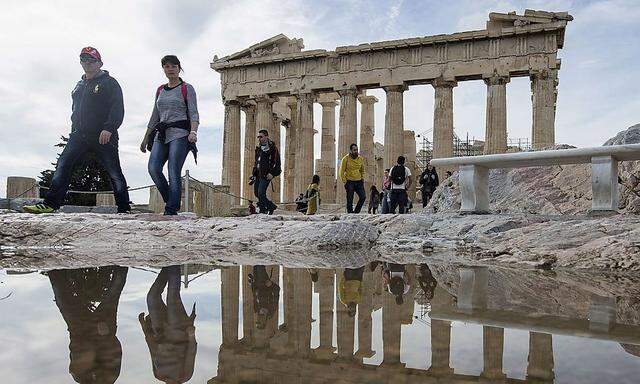 Tourists walk in front of the Parthenon Temple at the archaeological site of the Acropolis Hill in Athens