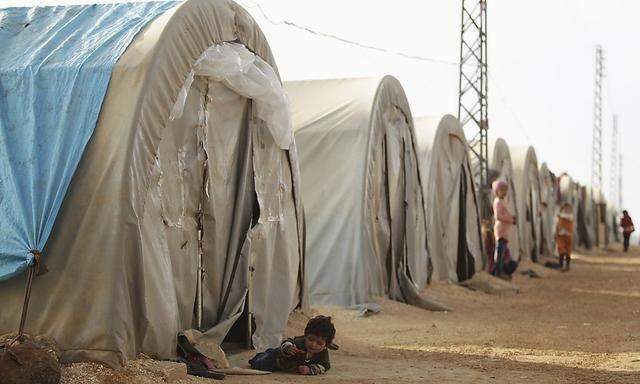 Children, who are internally displaced due to fighting between rebels and forces loyal to Syrian President Bashar al-Assad, wait outside tents at the Jarjanaz refugee camp in the southern countryside of Idlib