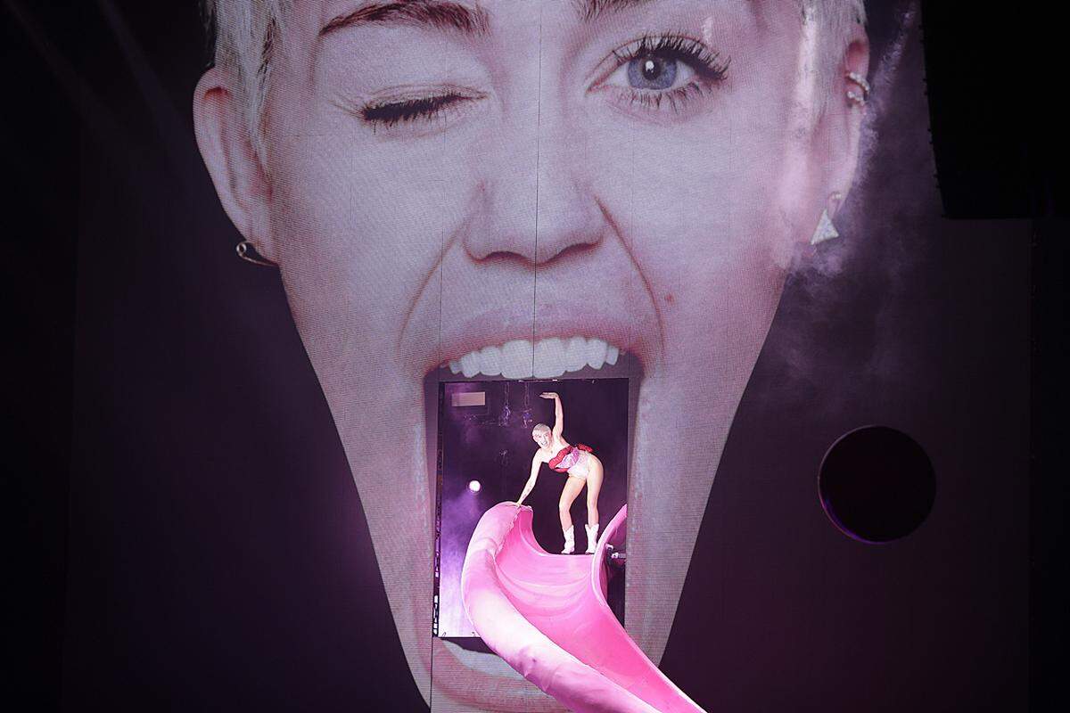 So beginnt die Bangerz-Show: Zuerst ist da ein riesiges Bild des Gesichts von Miley Cyrus. Dann klettert sie persönlich aus den eigenen Lippen und rutscht die eigene Zunge hinunter auf die Bühne.