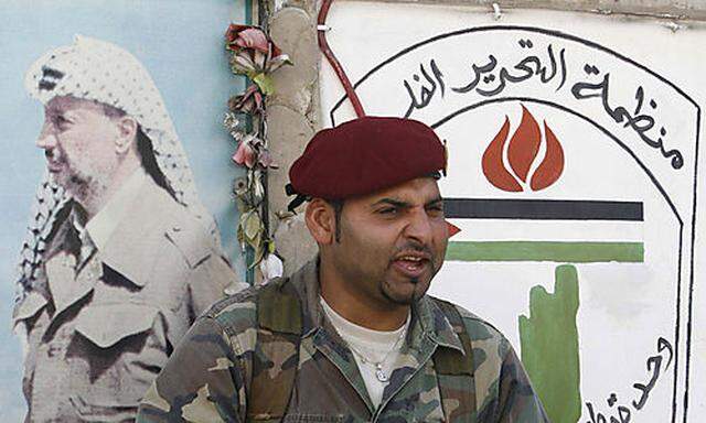 A Palestinian militant sits in front of a picture of late Palestinian leader Yasser Arafat in the Pal