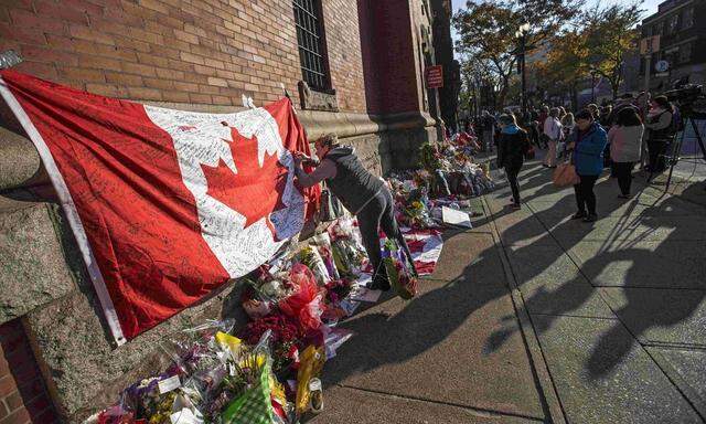 People write messages on a Canadian flag in a makeshift memorial in honour of Cpl. Nathan Cirillo, outside the Lieutenant-Colonel John Weir Foote Armoury in Hamilton