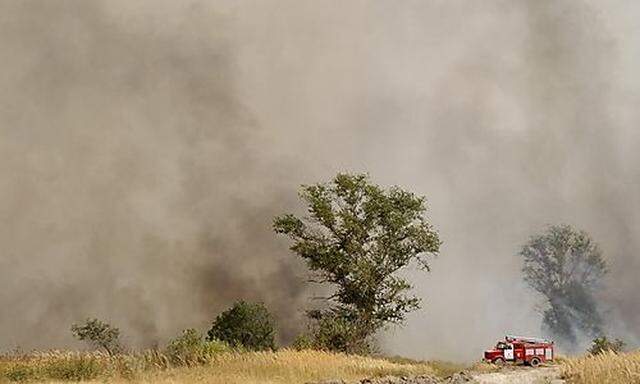 A fire engine waits along a road while smoke from a wildfire clouds the air outside the settlement of