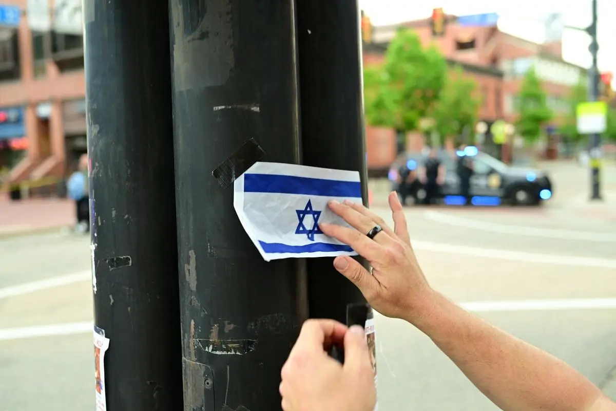 Sam King attaches an Israeli flag to a street lamp near the crime scene of an attack in which several people were injured, in Boulder
