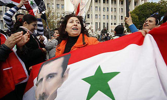 A woman holds a large Syrian flag at a rally in support of President Bashar Assad, pictured in the la
