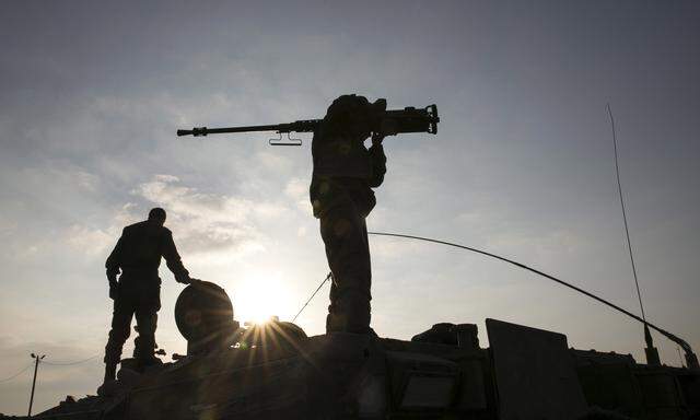 An Israeli soldier holds a weapon atop an armoured personnel carrier (APC) after crossing back into Israel from Gaza
