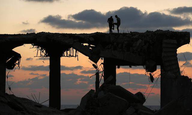 Palestinians stand atop a damaged building on a beach during sunset in the northern Gaza Strip
