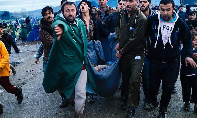 Flüchtlinge tragen eine verletzte Frau an der griechisch-mazedonischen Grenze.