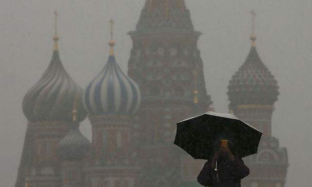 A man walks under an umbrella during a snowfall, with St. Basil's Cathedral seen in the background, in Red Square in central Moscow