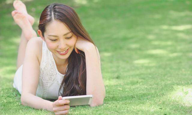 Portrait of young Japanese woman laying on grass with smartphone PUBLICATIONxINxGERxSUIxAUTxHUNxONLY