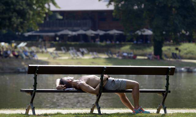 A man sleeps on a bench in a park during a heat wave