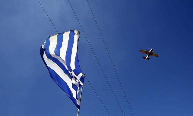 A firefighting aircraft flies over a Greek flag after dropping water at a forest fire in Marathon near Athens