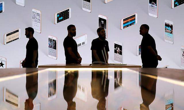 Store employees stand in front of a screen displaying iPhones during a preview event at the new Apple Store Williamsburg in Brooklyn, New York