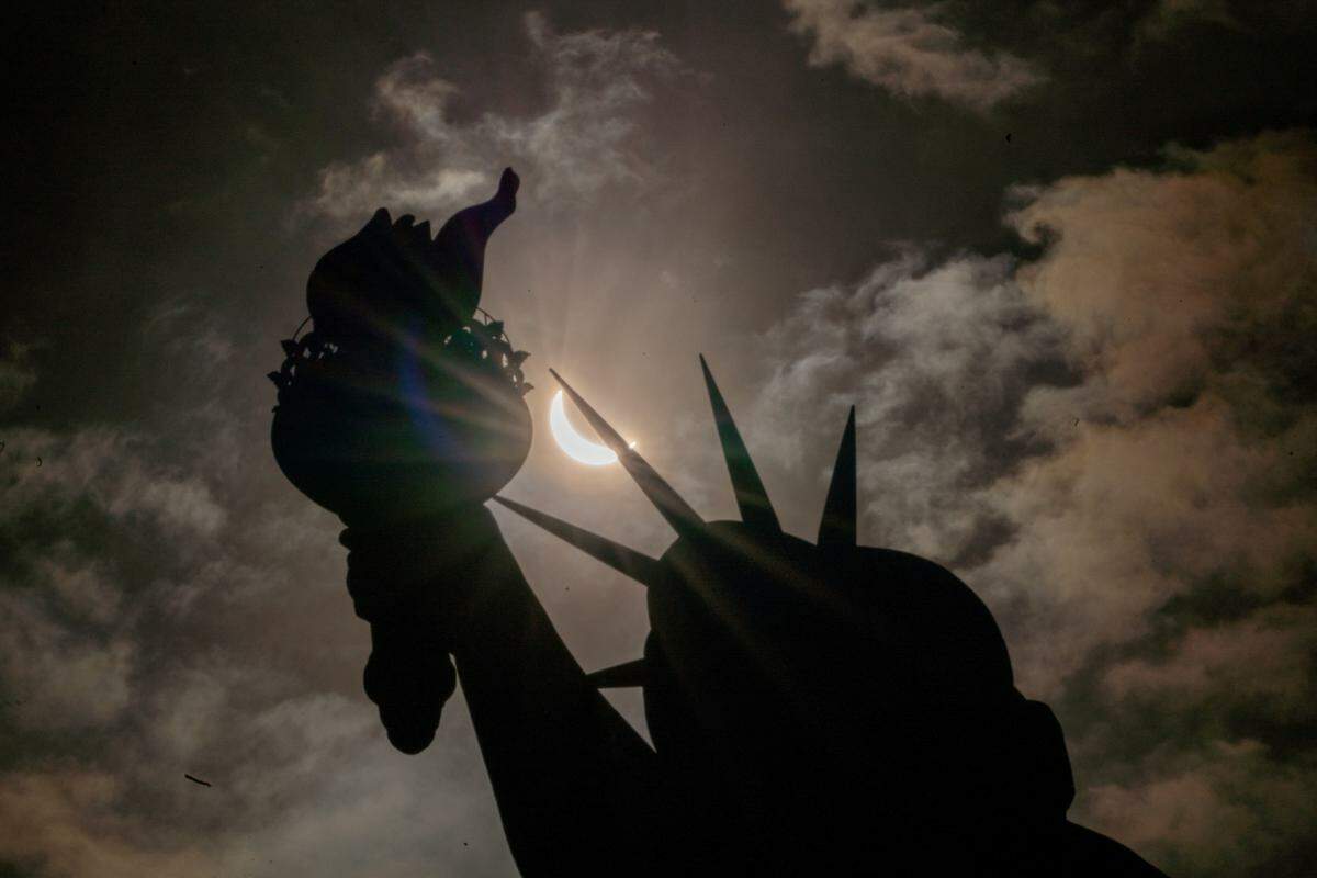 9. April. Die Freiheitsstatue während der Sonnenfinsternis auf Liberty Island in New York City.