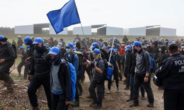 Die Aktivistinnen und Aktivisten schwenken blaue Flaggen bei ihrer Protestaktion nahe dem Gelände der Tesla-Fabrik in Grünheide.