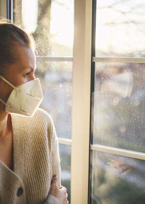 Pretty woman in quarantine with mask, looks out the window