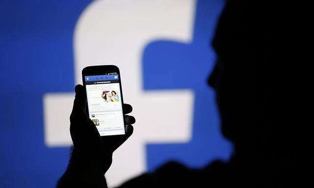 A man is silhouetted against a video screen with an Facebook logo as he poses with an Samsung S4 smartphone in this photo illustration taken in the central Bosnian town of Zenica