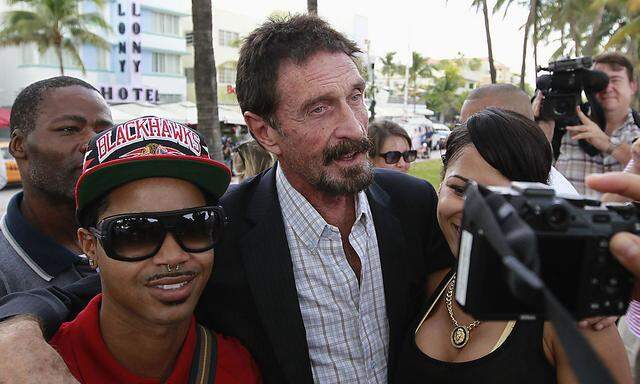 Computer software pioneer McAfee poses with tourists as he speaks with reporters outside his hotel in Miami Beach