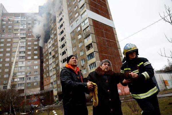 Feuerwehrmänner helfen einer Bewohnerin des von Russland attackierten Hochhauses in Kiew.