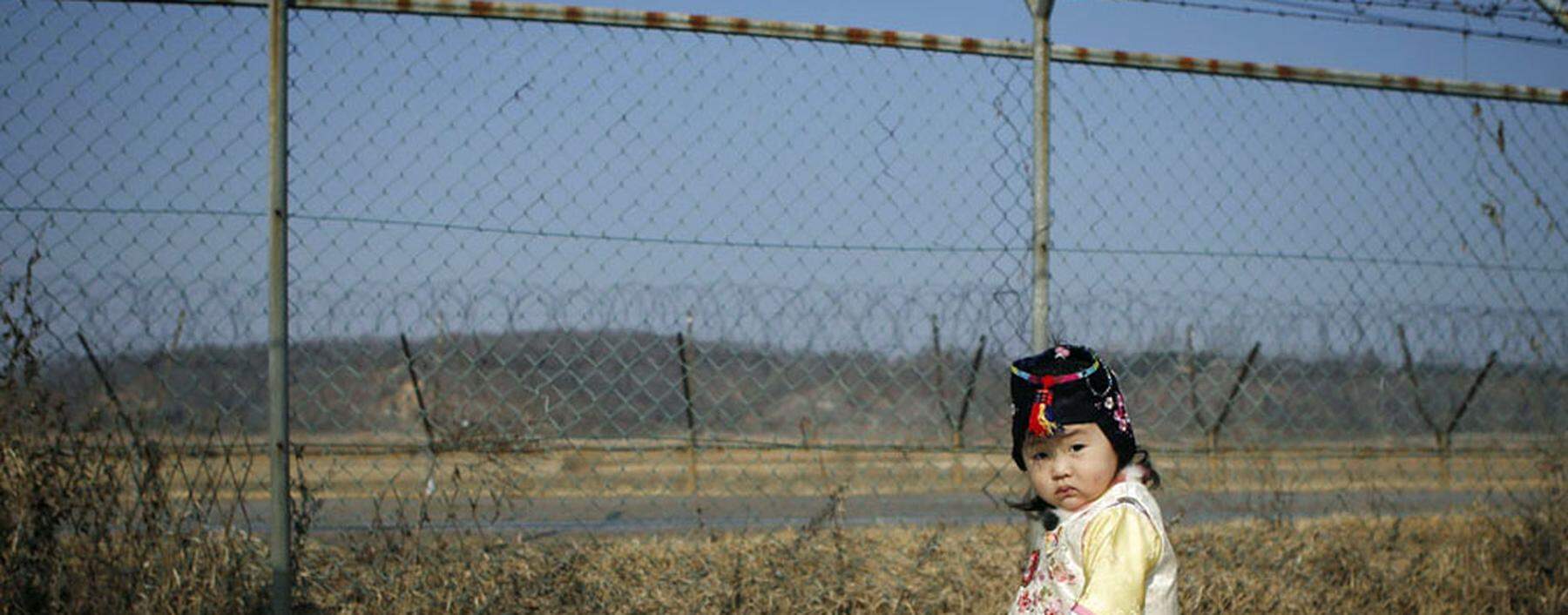 A girl dressed in a Hanbok, a Korean traditional costume, stands in front of a barbed-wire fence, as her parents prepare for a memorial service for North Korean family members, near the demilitarized zone separating the two Koreas, in Paju