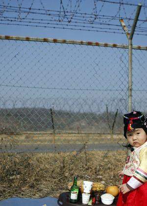 A girl dressed in a Hanbok, a Korean traditional costume, stands in front of a barbed-wire fence, as her parents prepare for a memorial service for North Korean family members, near the demilitarized zone separating the two Koreas, in Paju