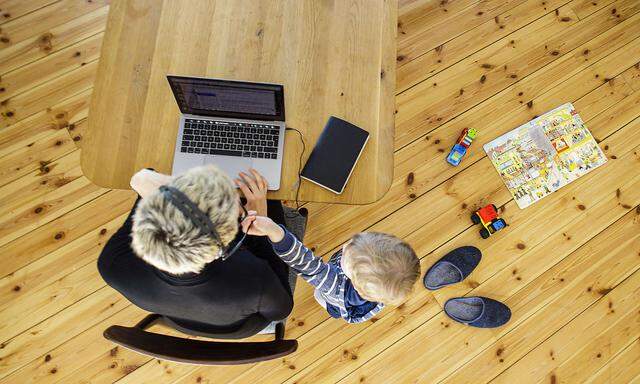 Symbolfoto zum Thema Homeoffice. Eine Frau sitzt zu Hause am Schreibtisch und arbeitet. Neben ihr spielt ein Kind. Berli