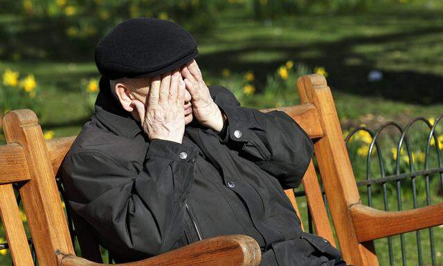 An elderly man rubs his face as he sits in the spring sunshine in St James´s Park in London