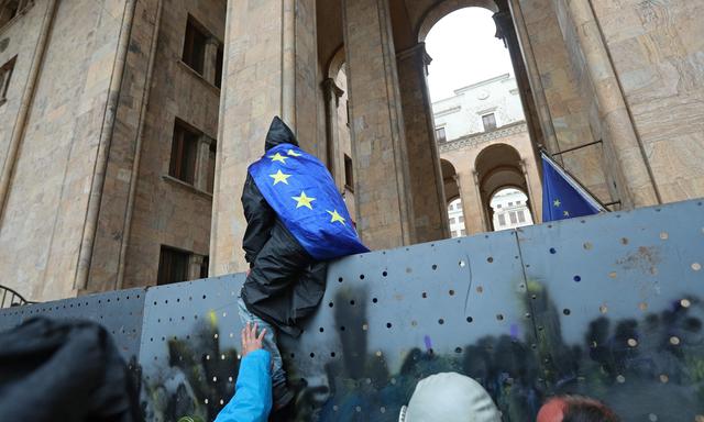 Ein Demonstrant klettert beim Parlament in Tiflis über eine Absperrung.
