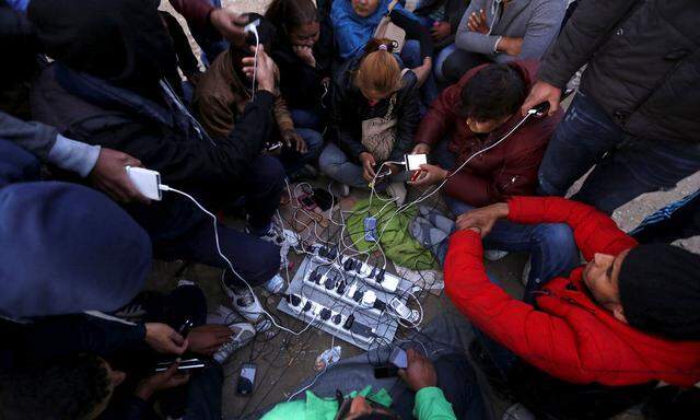 Stranded migrants charge their phones on a field with electricity provided by a generator at the Greek-Macedonian border near the Greek village of Idomeni