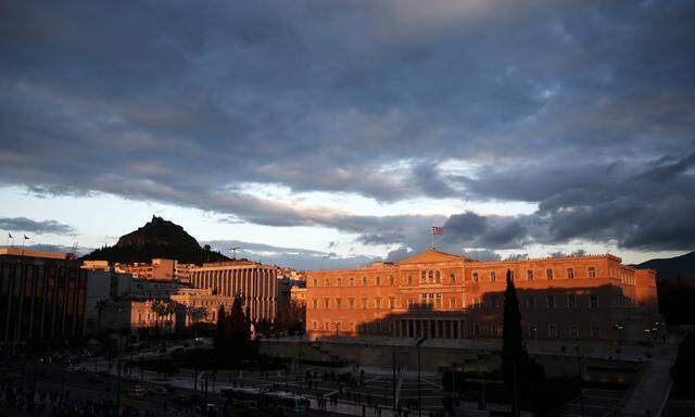 A Greek national flag flutters atop the parliament building during sunset in Athens
