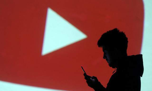 Silhouette of mobile user is seen next to a screen projection of Youtube logo in this picture illustration