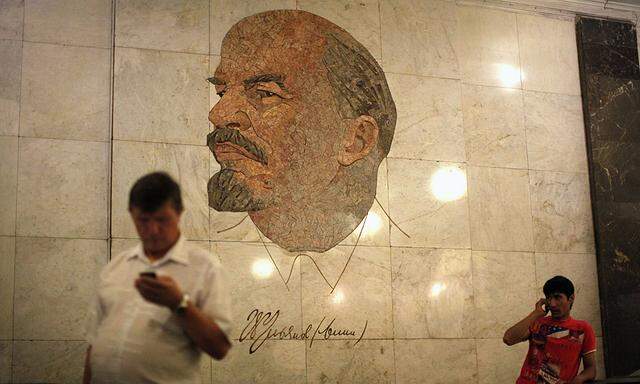 Men use their mobile phones as they stand in front of a mosaic depicting former Soviet leader Vladimir Lenin at Biblioteka Imeni Lenina metro station in Moscow