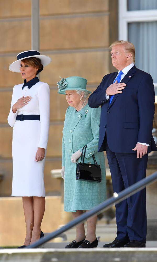 Hand aufs Herz: Weißes Kleid (von Dolce &amp; Gabbana), lange Ärmel, dunkler Taillengürtel und Schuhe, das haben wir doch schon einmal ganz ähnlich gesehen - und zwar an Herzogin Meghan beim Pferderennen in Ascot. Ob sich Queen Elizabeth II wohl das gleiche gedacht hat?