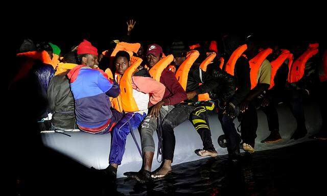 Migrants gesture from a rubber boat before being rescued during a search and rescue operation by the NGO Proactiva Open Arms rescue boat in the central Mediterranean Sea