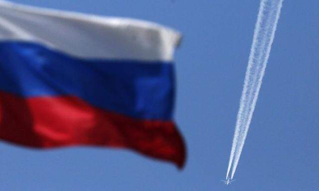 A contrail left by a passenger plane is seen behind a Russian state flag as it passes over the Siberian city of Krasnoyarsk