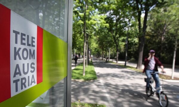 A cyclist talks on his mobile phone as he passes a Telekom Austria phone booth in Vienna