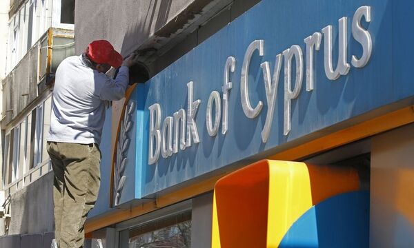 A worker paints a wall above a branch of Bank of Cyprus in Bucharest