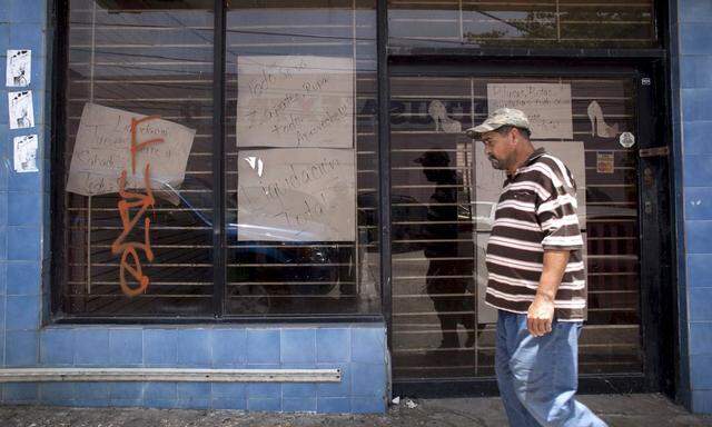 A man walks past a closed store with signs reading 'Closing down sale' and 'Everything goes, shoes, clothes, take advantage' in Arecibo, Puerto Rico