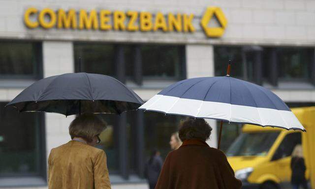People with umbrellas walk past a Commerzbank branch in Frankfurt