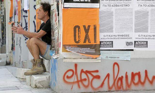 A man sits on a building entrance, next to a referendum campaign poster with the word 'No' in Greek in Athens