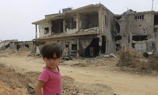 A child is seen in front of a damaged house in Qusair