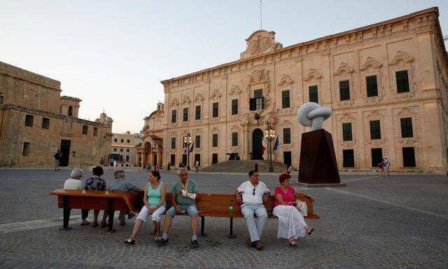 Elderly people sit on a bench in front of the Auberge de Castille in Valletta