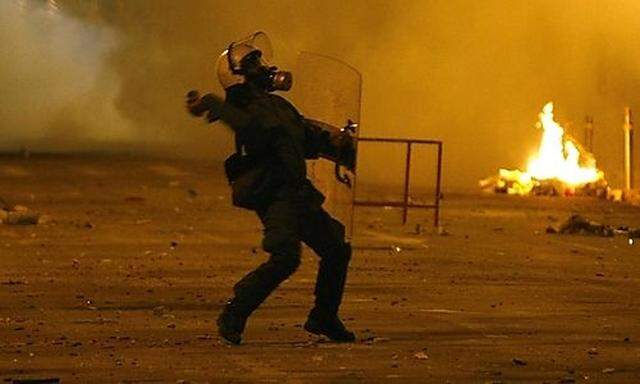 A policeman throws a teargas canister against protesters outside the Athens Law university Law university