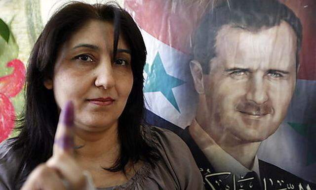 Eine Frau zeigt ihren von der Wahl gefärbten Finger, hinter ihr prankt das Konterfei des Präsidenten Assad
