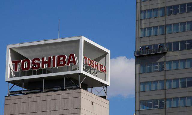 The logo of Toshiba Corp is seen as Window cleaners work on the company's headquarters in Tokyo