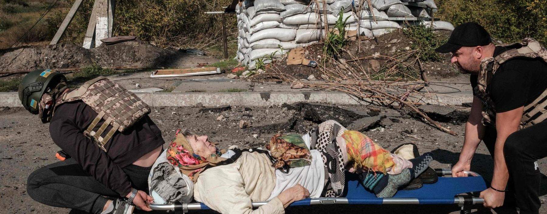 Nach dem Abzug der russischen Truppen versorgen ukrainische Freiwillige die Zivilisten in den befreiten Gebieten. Auf einer Trage wird eine 86-Jährige über die Brücke beim Fluss Oskil gebracht.