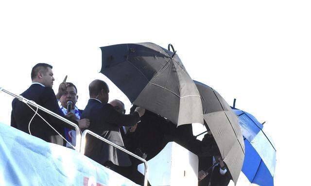 Istanbuls Bürgermeister Ekrem Imamoğlu wird mit Regenschirmen vom Steinhagel beschützt, er bricht einen  Wahlkampfauftritt ab.