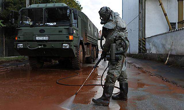A Hungarian soldier, wearing a chemical protection gear, cleans a street flooded by toxic in the town