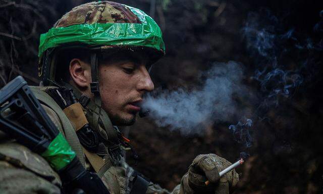 Ukrainian service member smokes in a trench at a position near the frontline town of Bakhmut